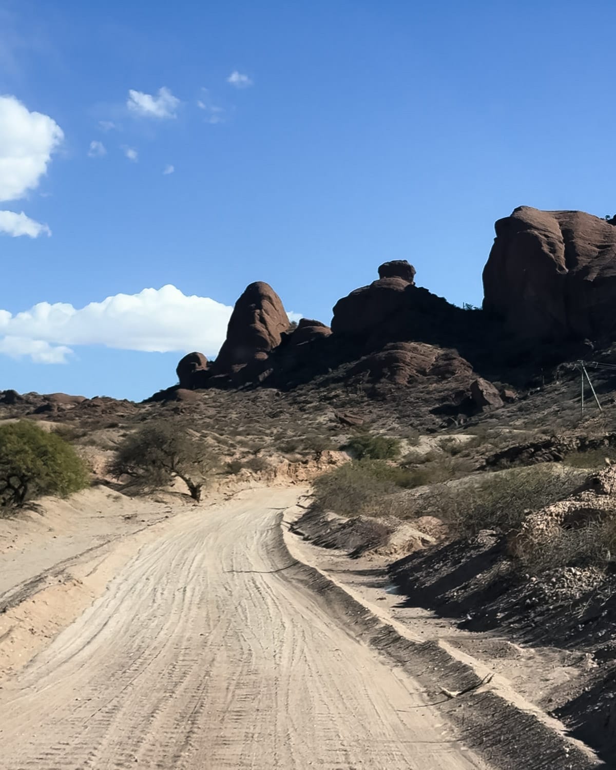 Winding sand road leading past red rock formations and sparse desert vegetation to Bodega Colome.