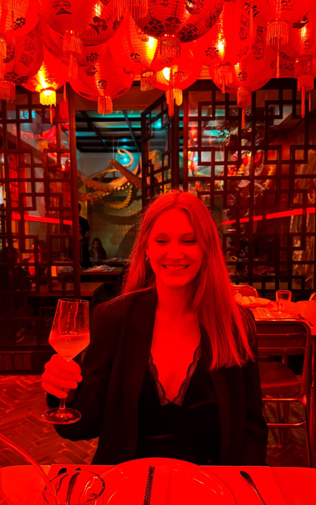 Cec smiling with a glass of wine inside Niño Gordo restaurant in Buenos Aires under glowing red lanterns.