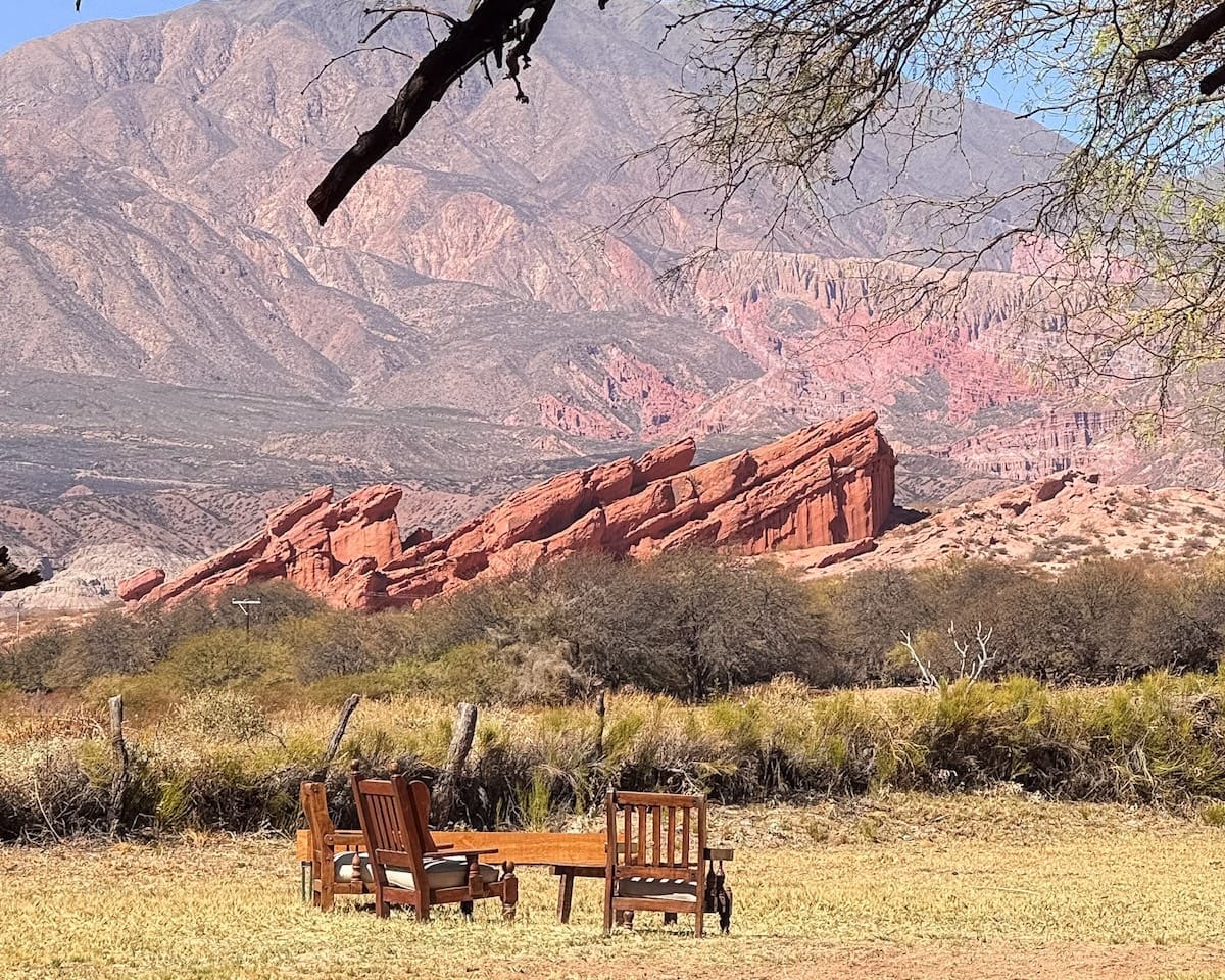 Wooden chairs and table set in front of dramatic red rock formations in the Quebrada de las Conchas at Santa Elena ranch.