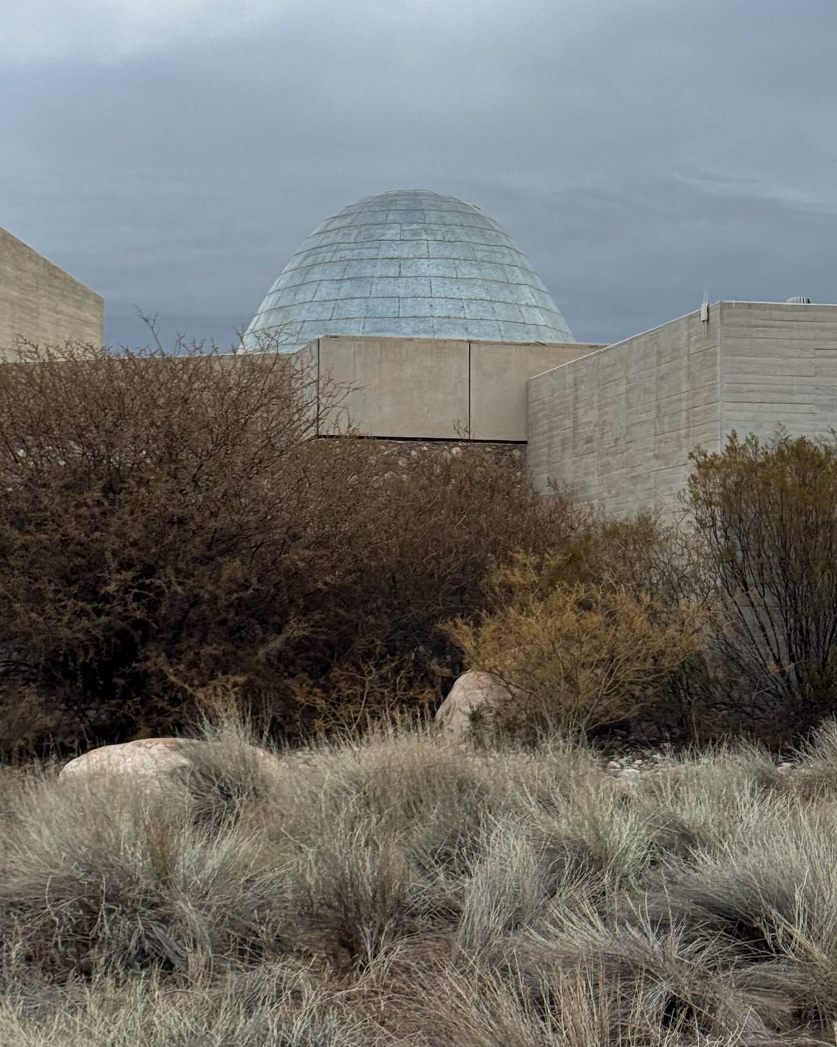 Exterior of Bodega Zuccardi in the Uco Valley, showing its dome-shaped roof emerging from native desert vegetation.