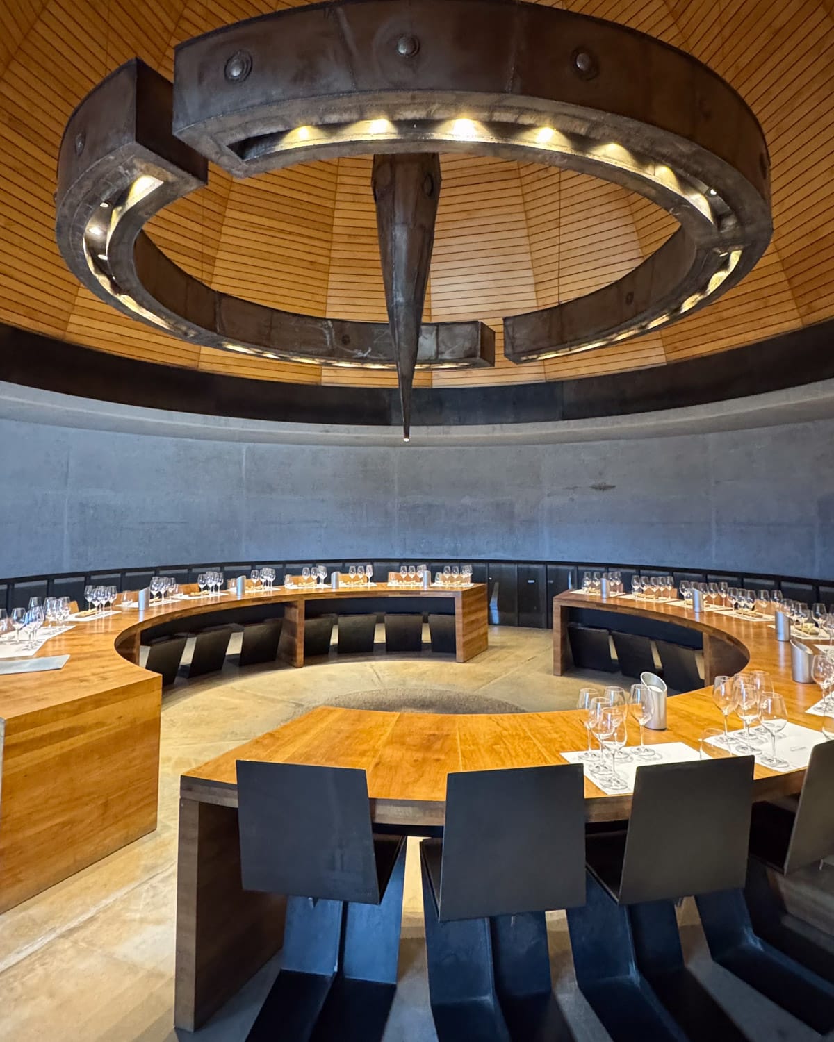 Circular wooden tables set with wine glasses inside the modern stone-walled tasting room at Zuccardi winery.