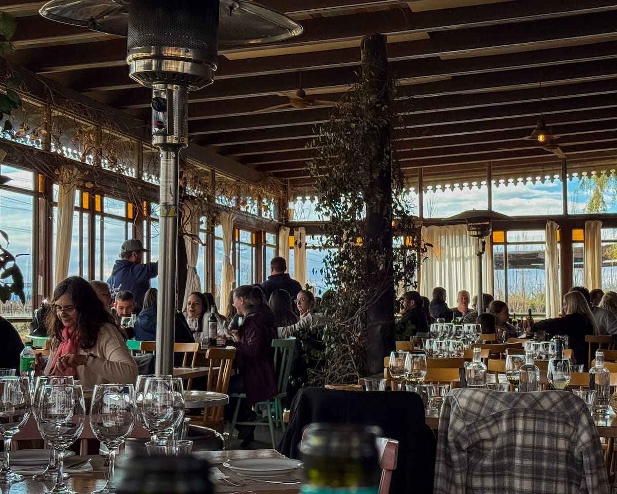 Busy interior of La Azul's winery restaurant filled with guests dining among glass windows and vineyard and mountain views.