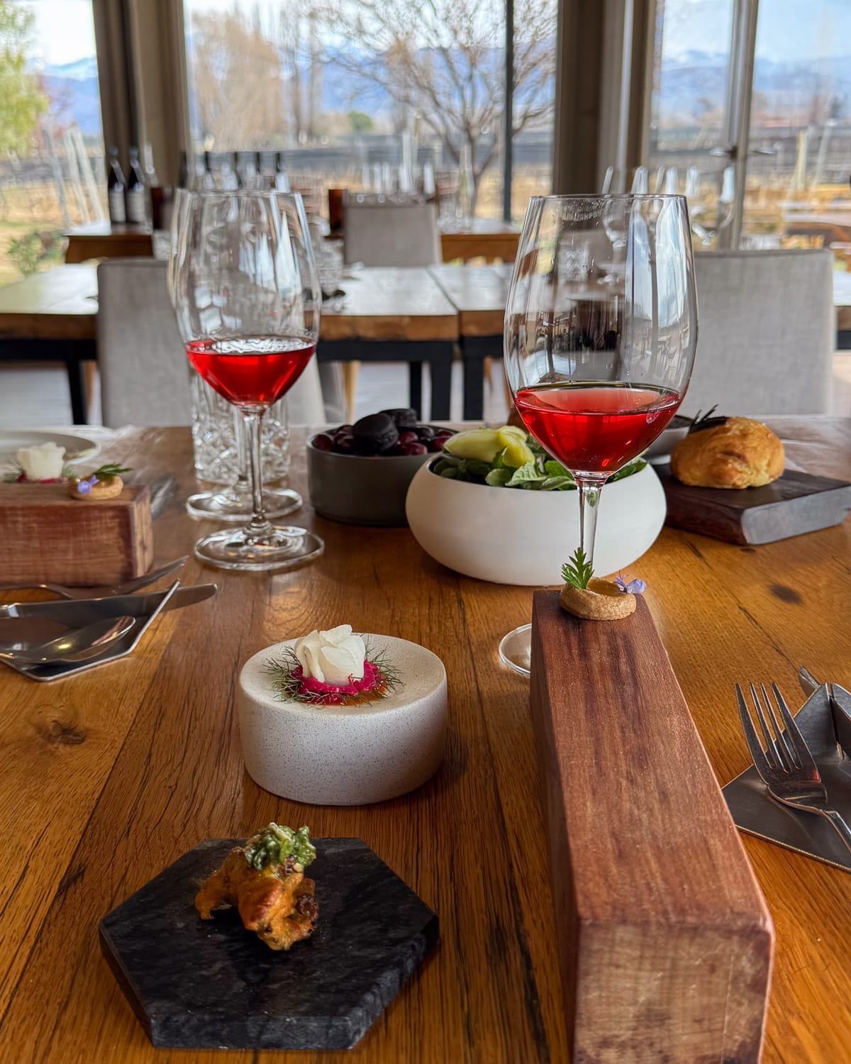 Elegant lunch setting at Riccitelli Bistro in Mendoza with rosé wine glasses, small plates, and vineyard and Andes views in the background.