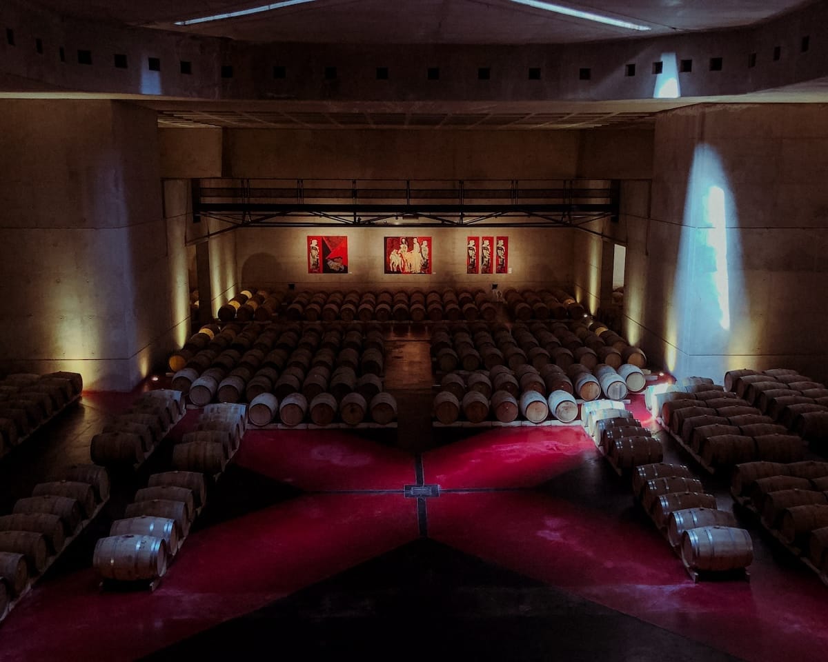 Wine cellar at Bodega Alfa Crux with rows of oak barrels and warm lighting shining through a concrete space.