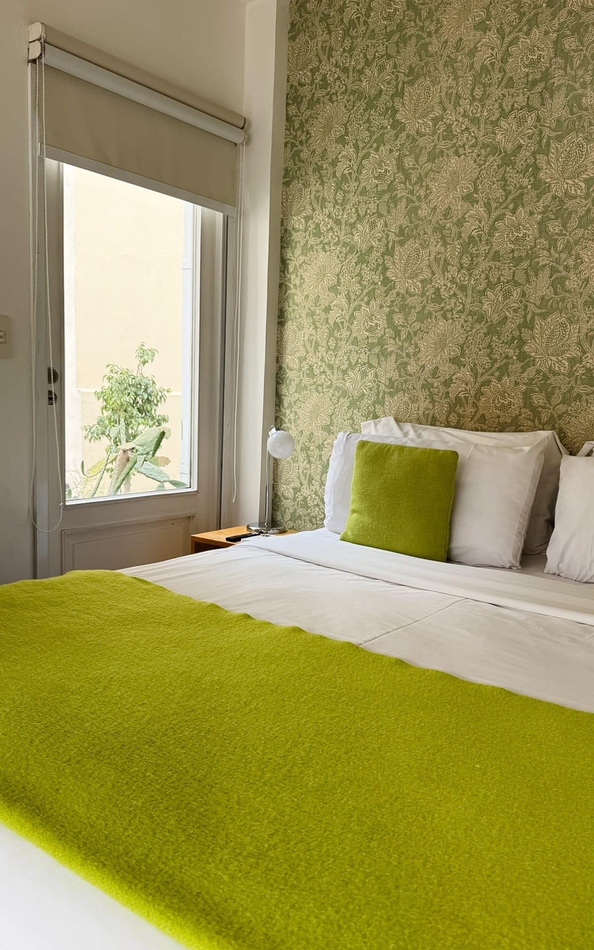 Bright hotel room at Home Hotel Buenos Aires with green wallpaper and white linens with green accent blankets and pillows.