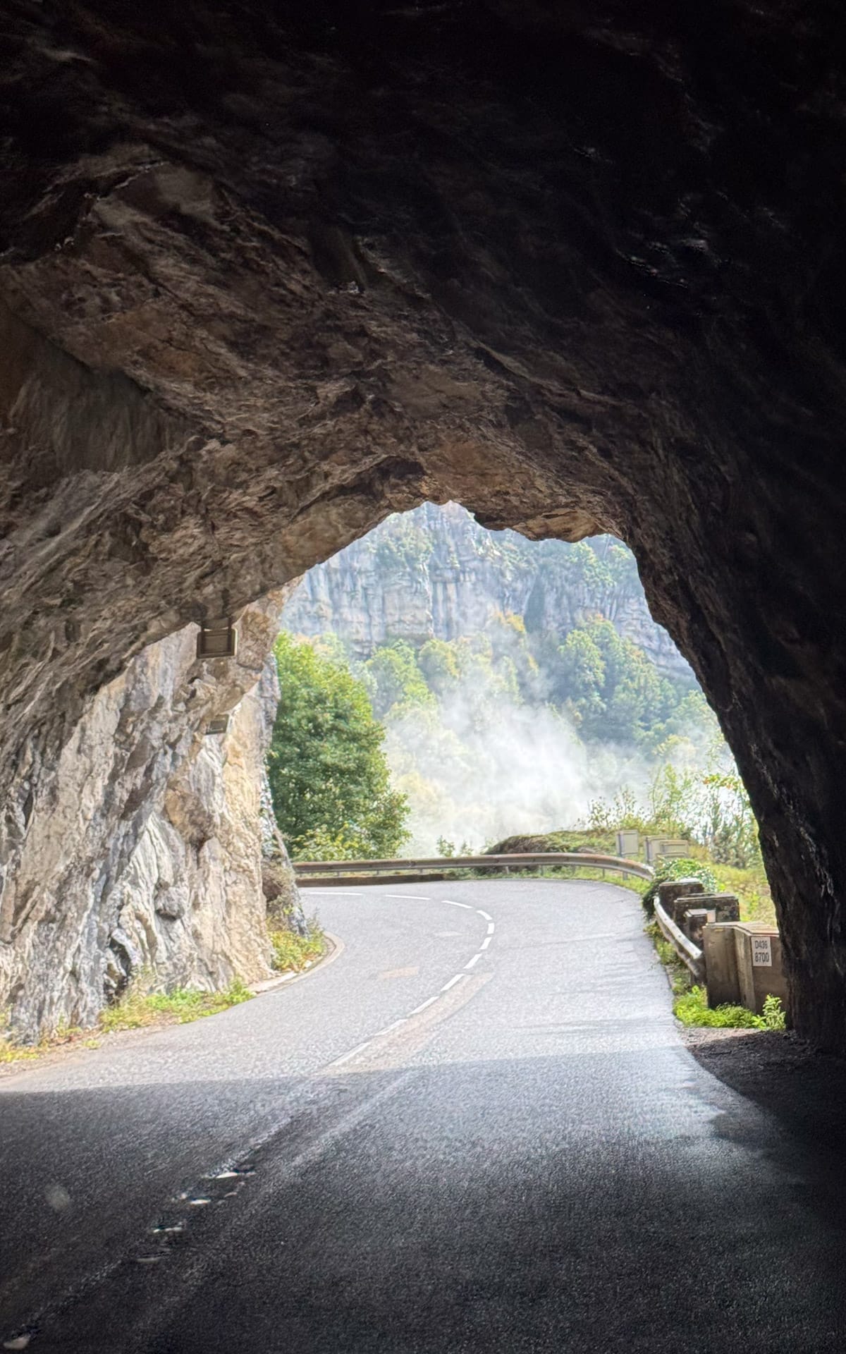 Mountain road passing through a rock tunnel in Parc naturel régional du Haut-Jura.