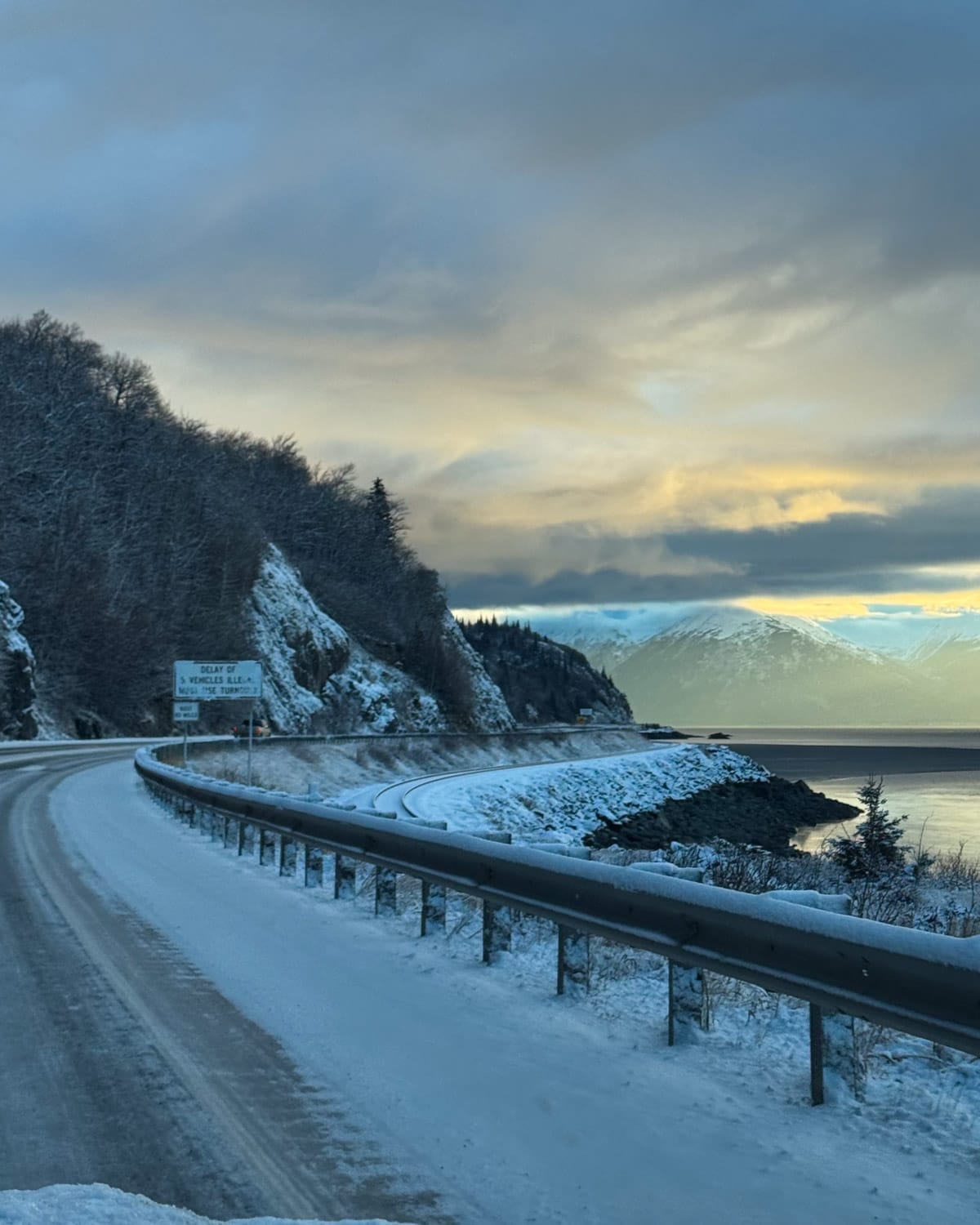 Winter drive along Seward Highway with golden sunlight hitting snow-dusted cliffs above Turnagain Arm in Alaska.
