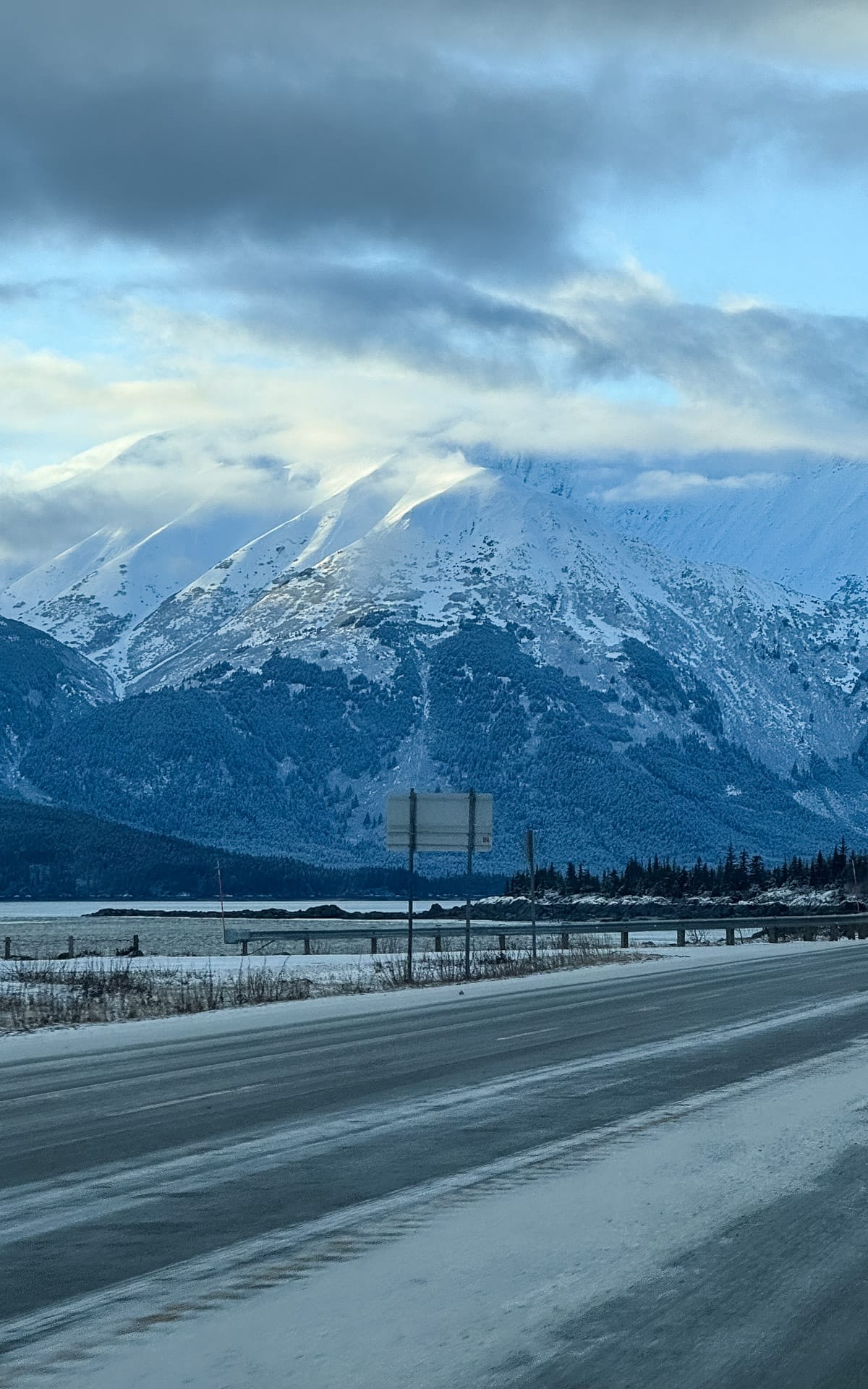 Snowy mountain range across Turnagain Arm viewed from the Seward Highway, with low clouds hanging over the peaks.