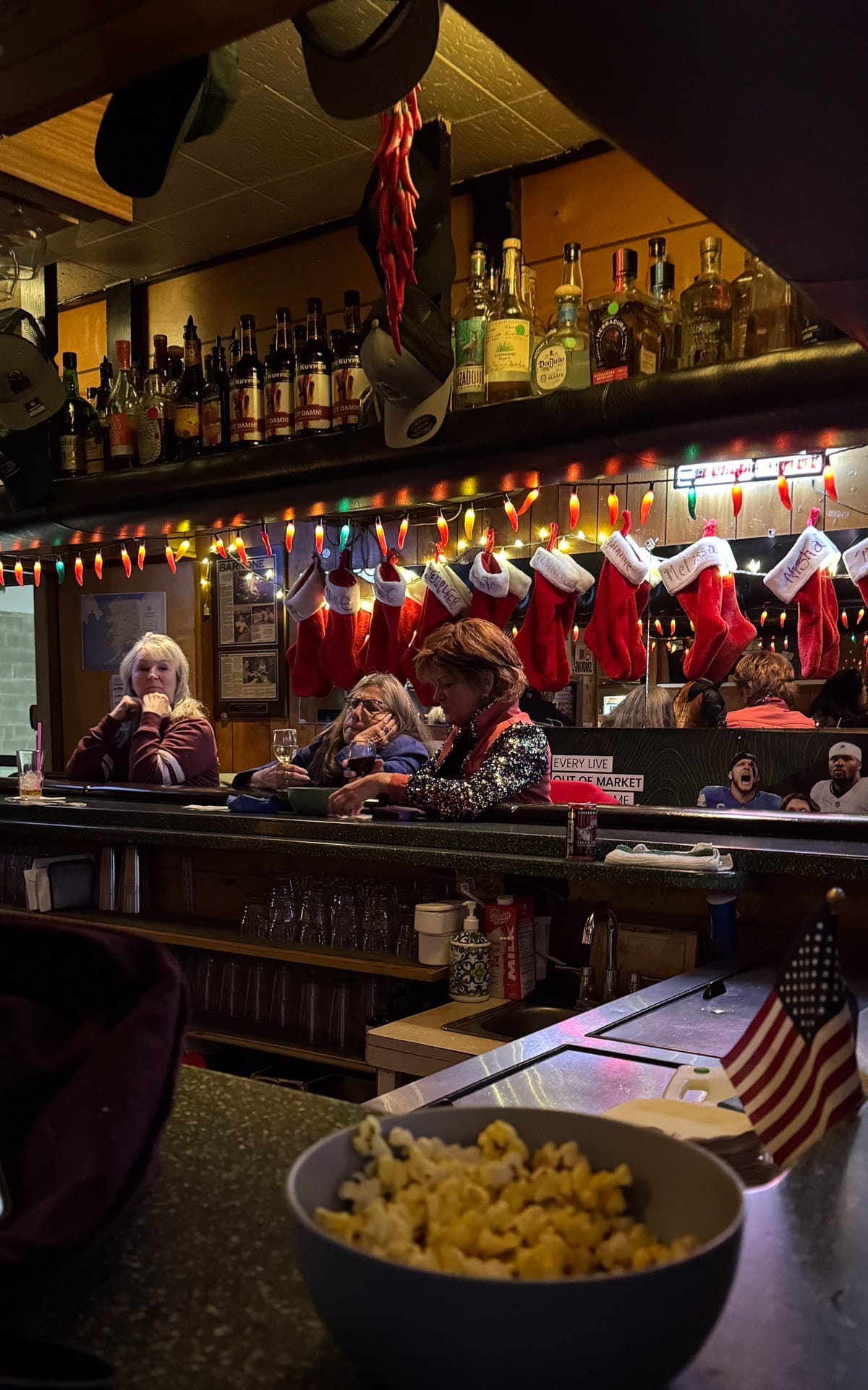 Bowl of popcorn on a bar counter at Darwin's Theory with holiday stockings and locals seated behind it.