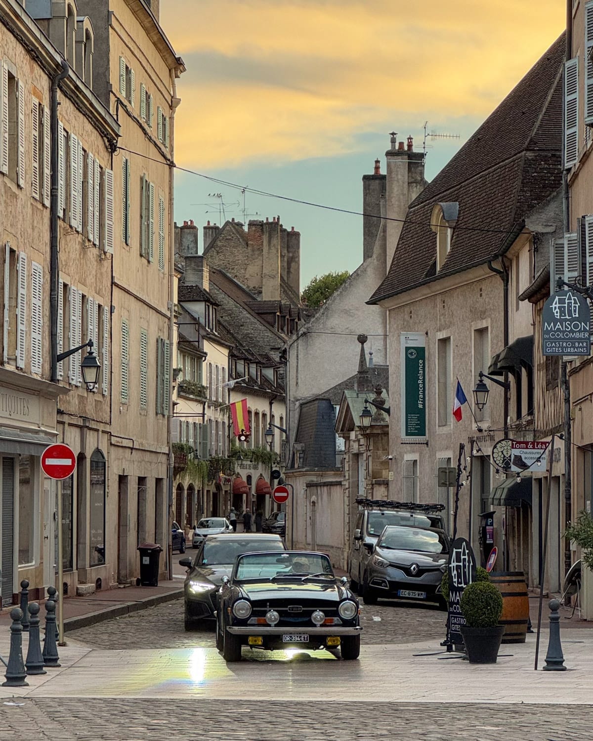 Classic car driving through Beaune’s old town streets at sunset.