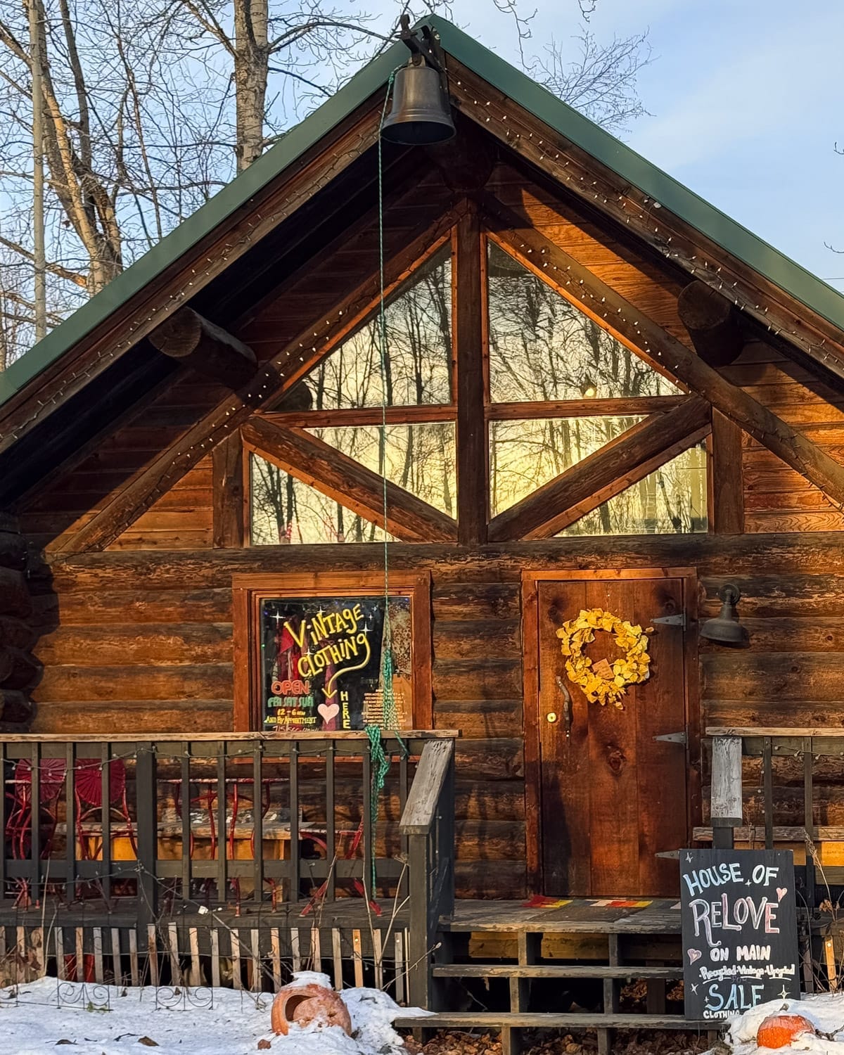 Rustic log cabin storefront in Talkeetna with a vintage clothing sign and wreath on the wooden door during winter.