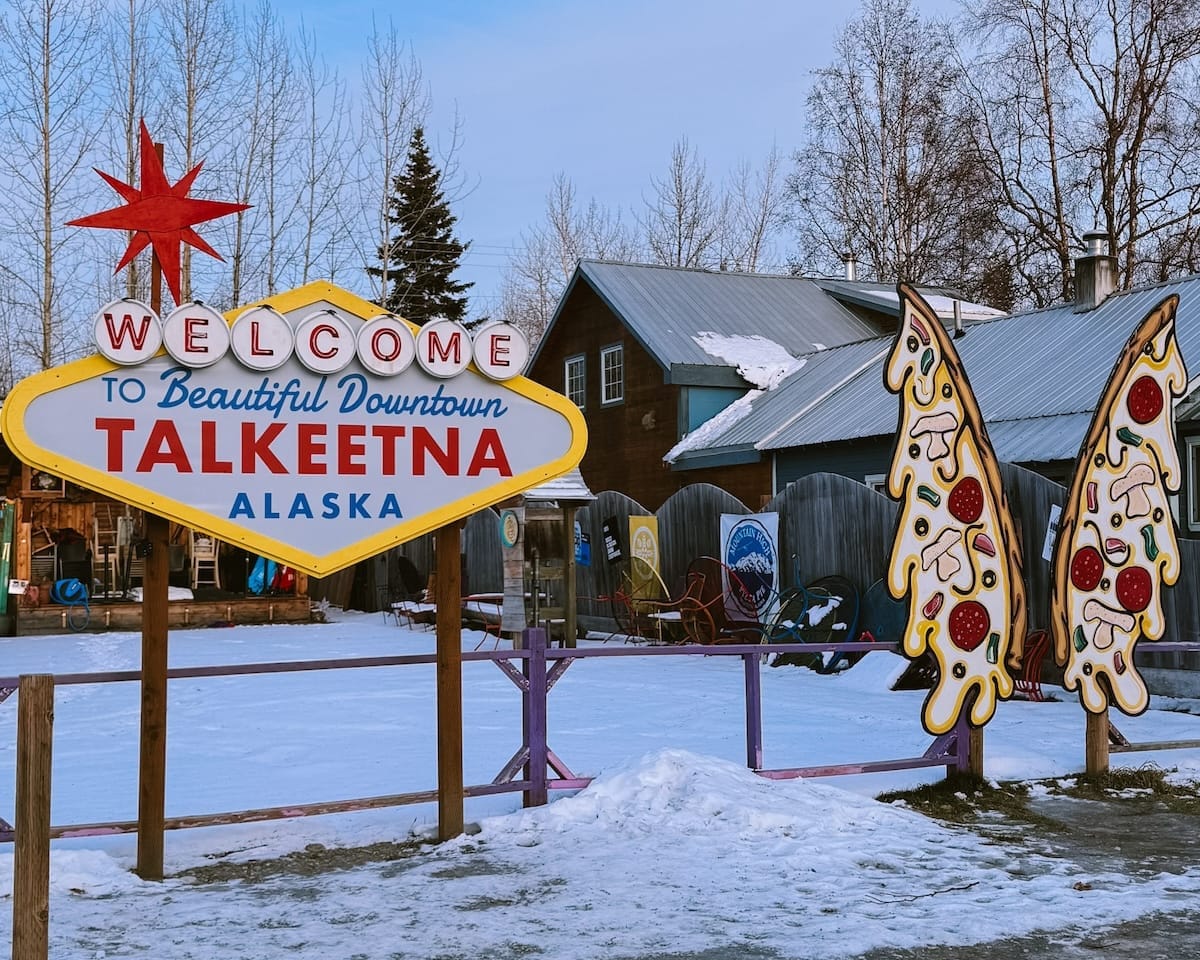 A Vegas style Welcome to Talkeetna sign and a pizza butterfly cutout for photos beside it.