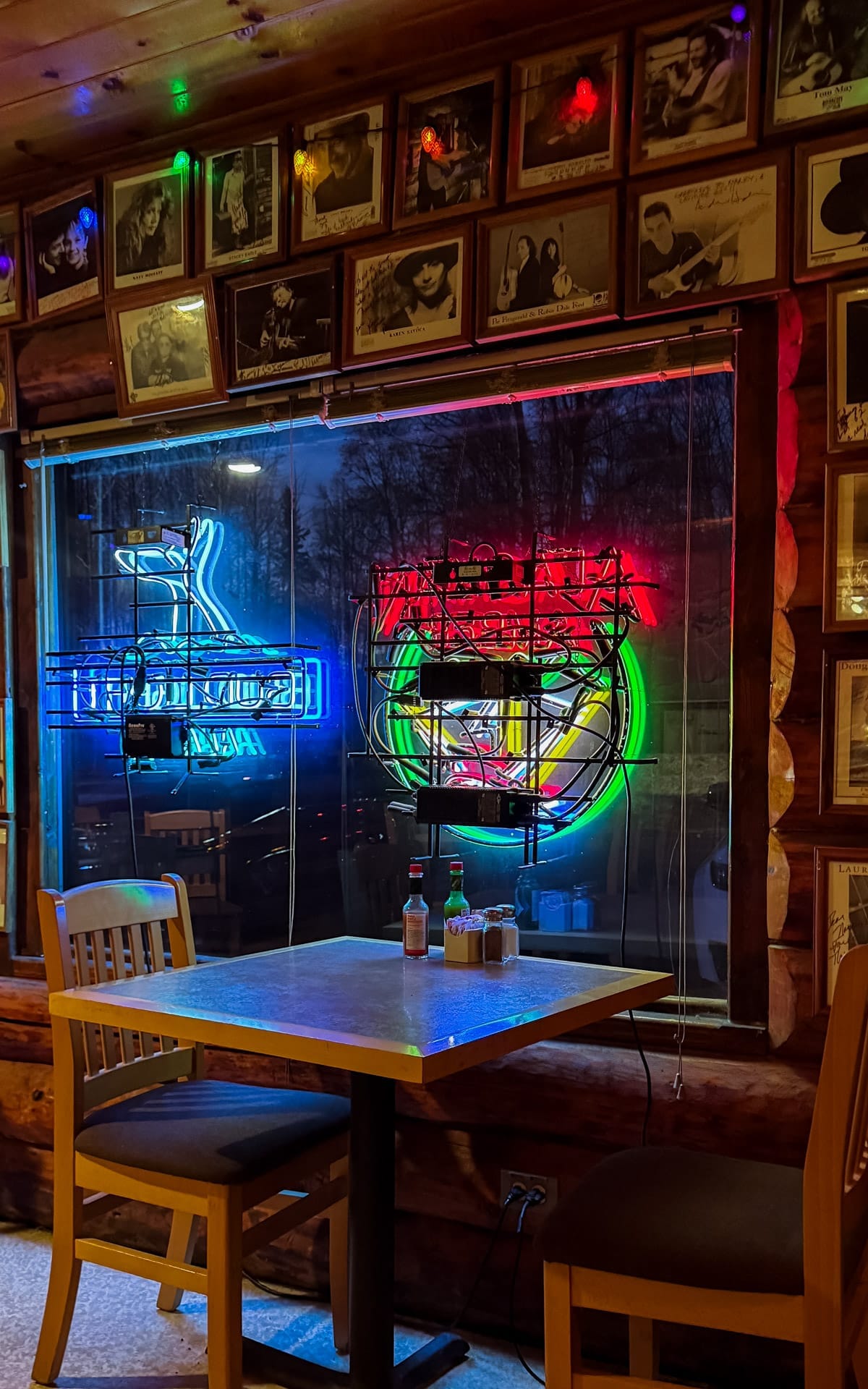 Bright neon beer signs glowing in the window of a rustic wooden restaurant at Latitude 62 with framed musician portraits lining the walls.