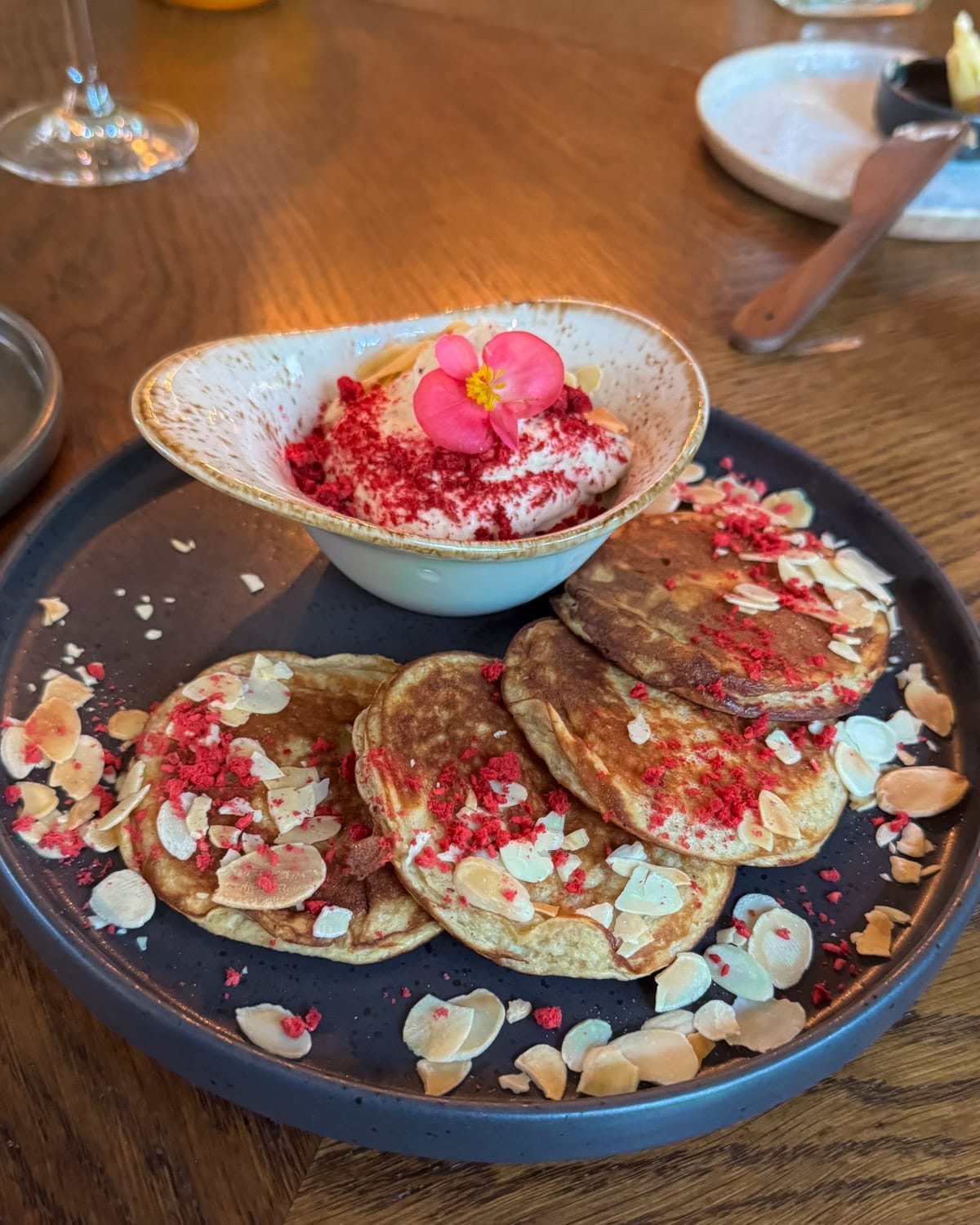 Banana pancakes topped with almonds and dried berries served with cream and edible flower garnish.