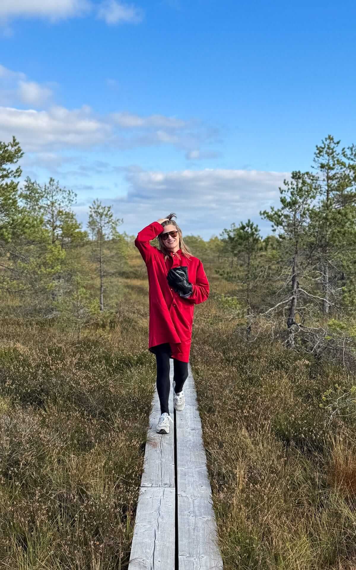 Cec walking along narrow wooden boardwalk through an Estonian bog to Loosalu Jarv, surrounded by low shrubs and pines.