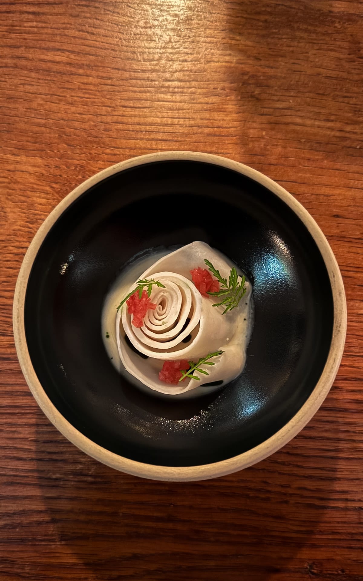 Fine-dining tasting menu course plated in a black bowl with delicate garnishes from SOO Restaurant.