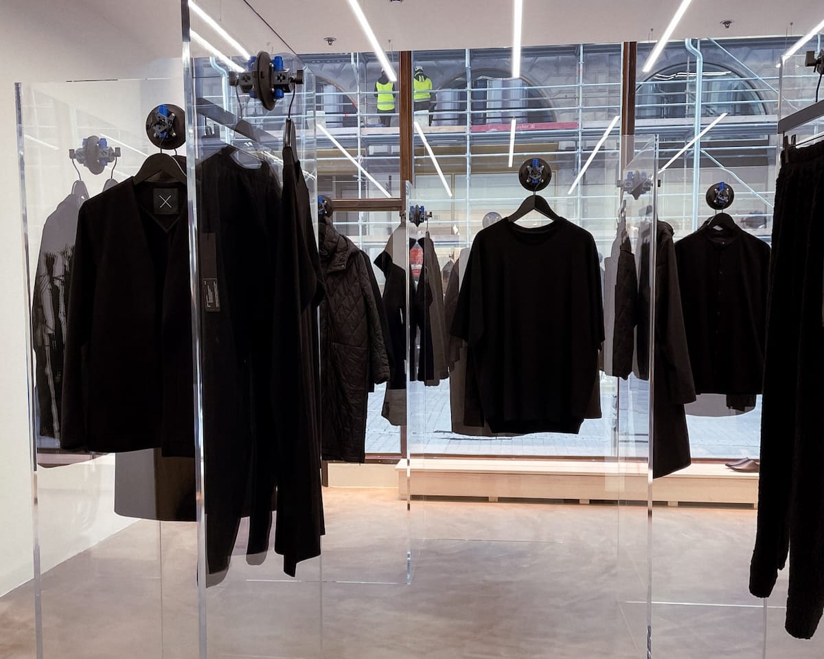 Minimal black clothing displayed inside Nomen Nescio boutique in Helsinki’s Design District, with sleek glass partitions and modern lighting.