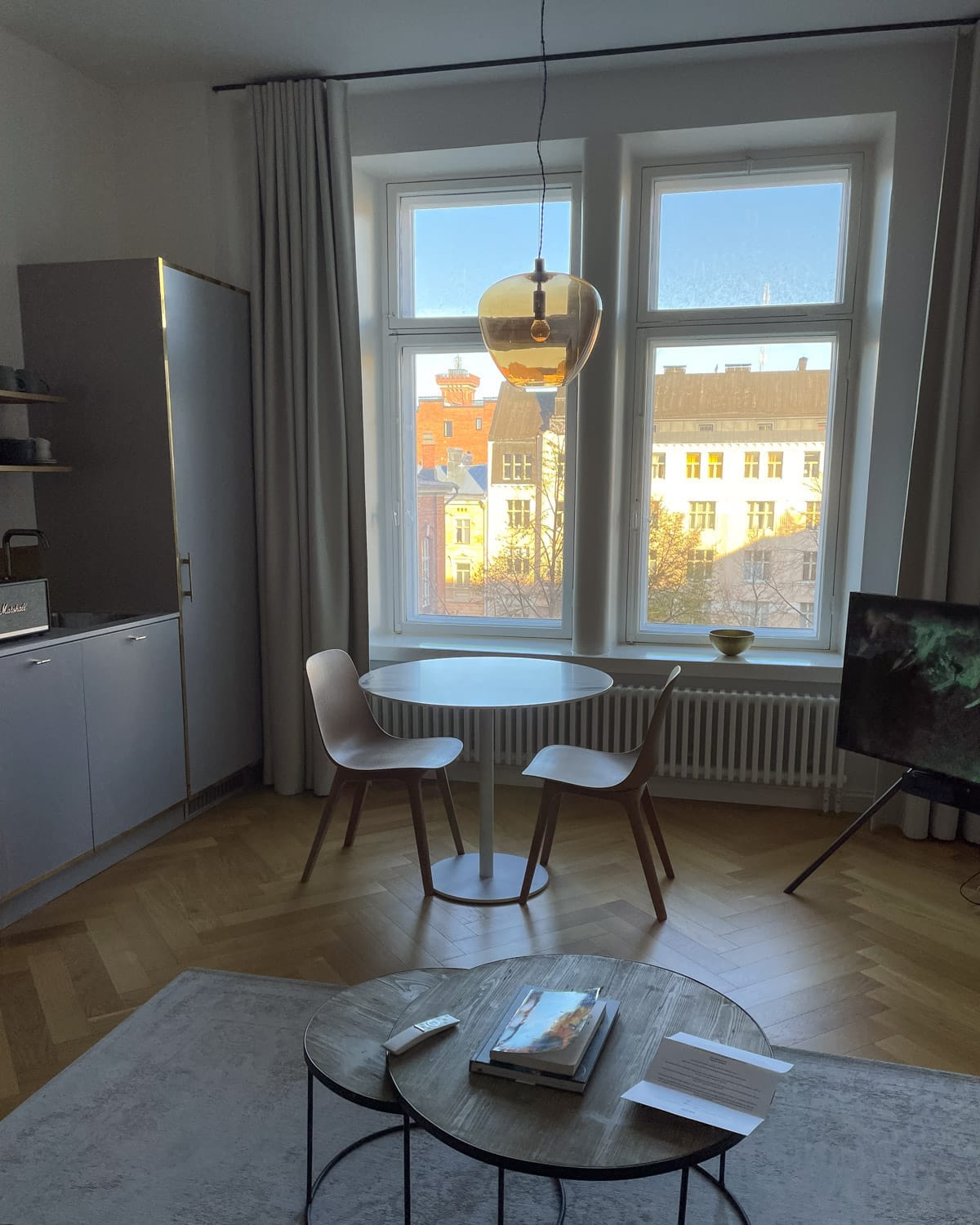 Minimalist Nordic apartment interior with round dining table, wooden chairs, and large windows overlooking Helsinki rooftops.