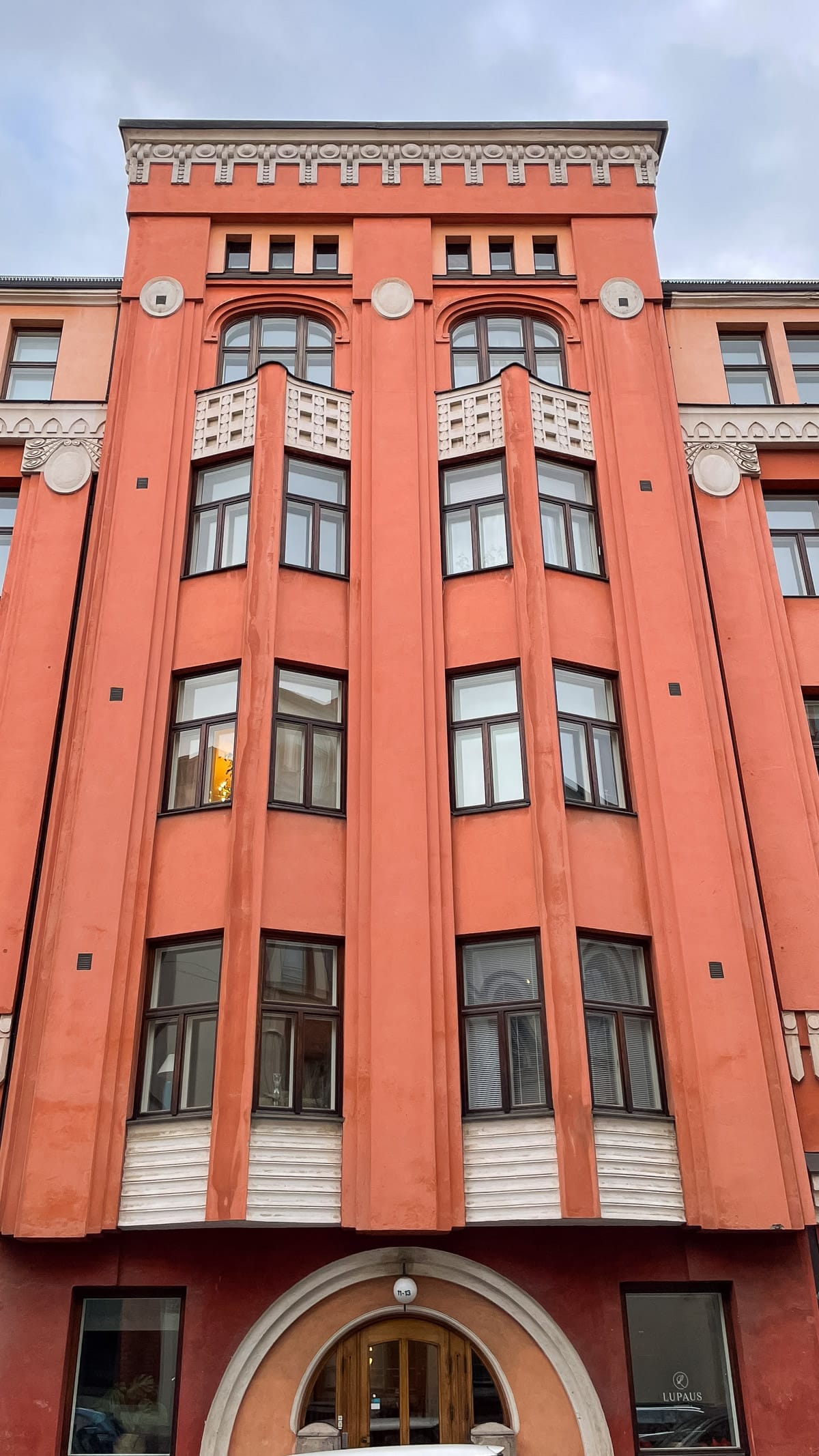 Coral-coloured Art Nouveau building in Helsinki with curved bay windows and decorative stone details.