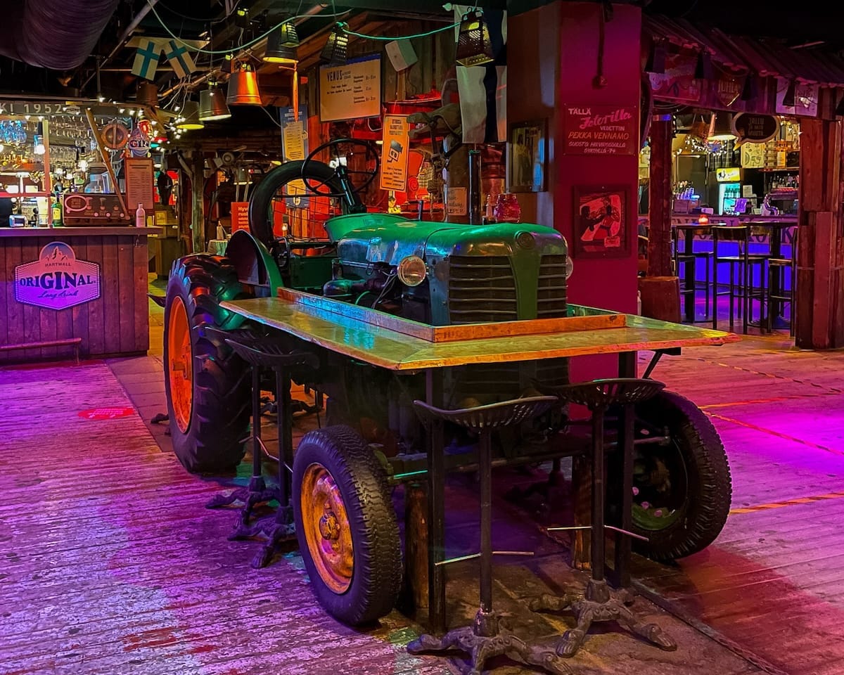 Eclectic Zetor bar interior with a vintage green tractor displayed as a table under colourful neon lighting.