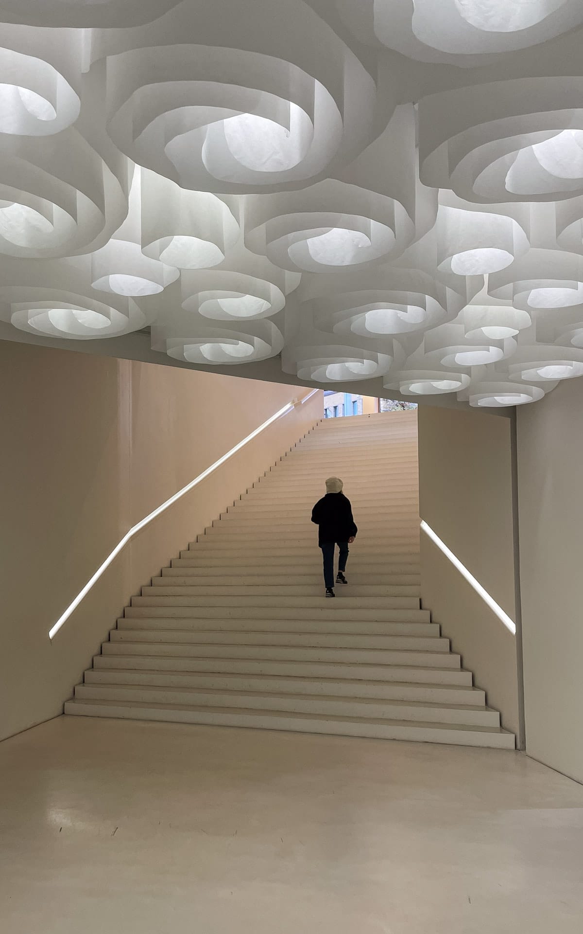 Curved white staircase at Amos Rex museum in Helsinki, with sculptural circular ceiling lights above.