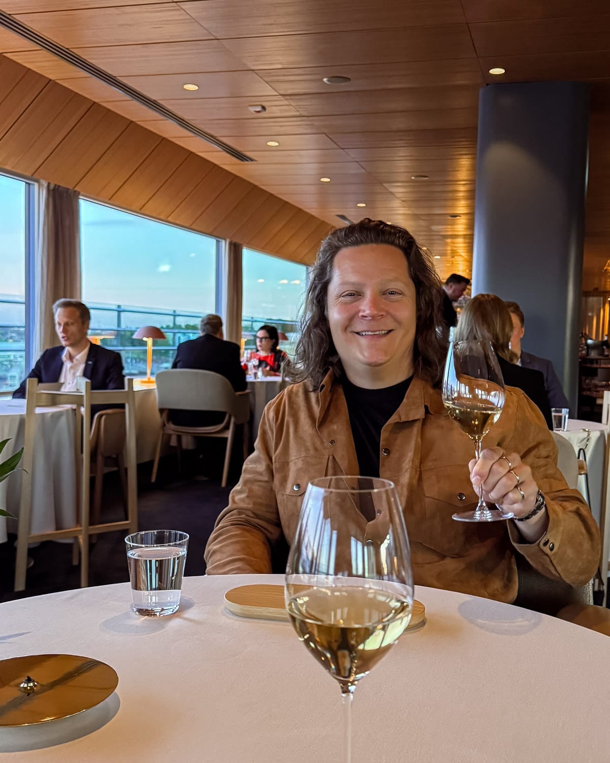 Ari holding a glass of champagne at Palace restaurant in Helsinki overlooking the Baltic Sea at golden hour.