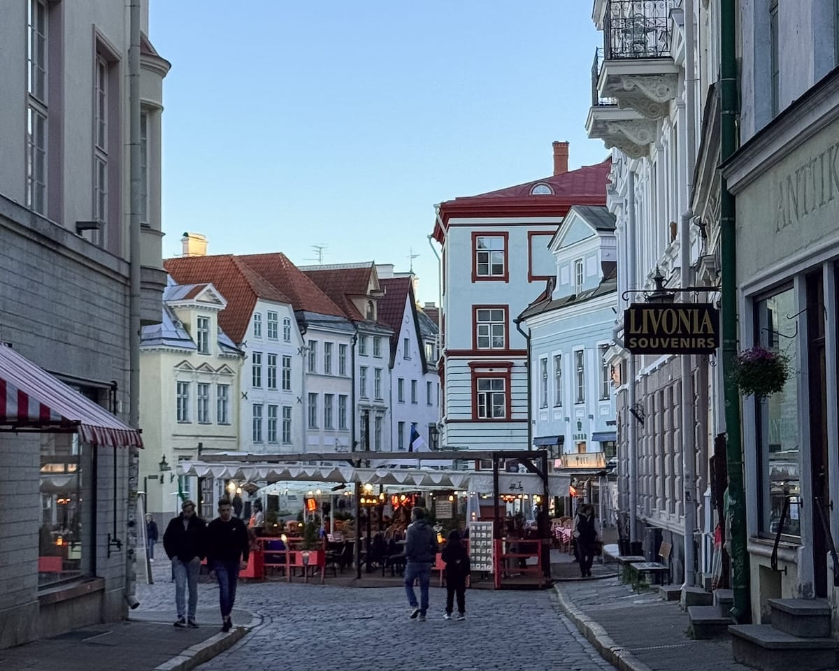 Evening scene of a cobblestone street in Tallinn’s Old Town with pastel façades and outdoor restaurant seating.