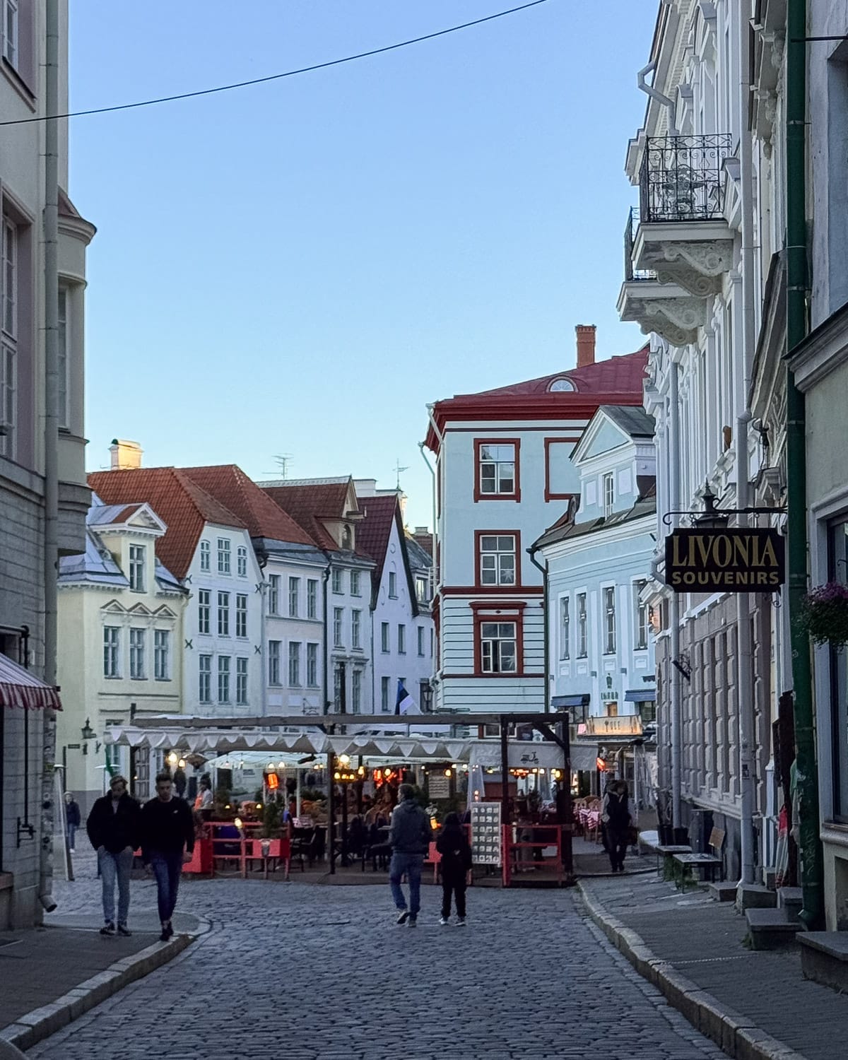 Evening scene of a cobblestone street in Tallinn’s Old Town with pastel façades and outdoor restaurant seating.