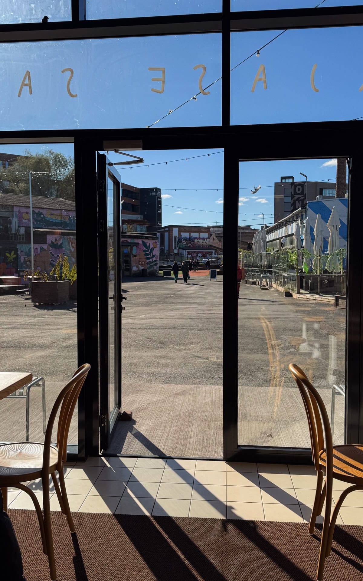View through Karjase Sai cafe's doors onto Telliskivi Creative City courtyard with murals and string lights.