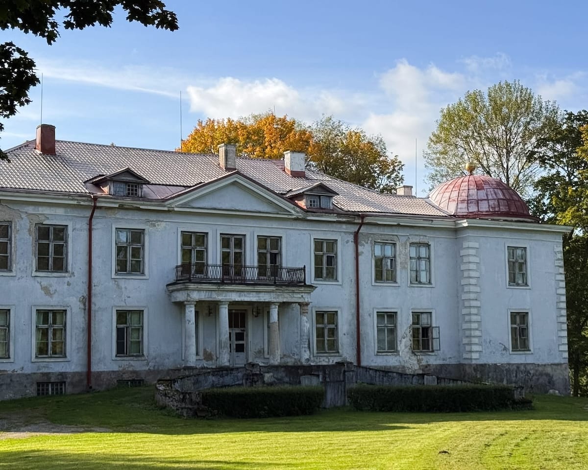 Weathered historic manor house with red dome roof set on manicured lawn in the countryside.