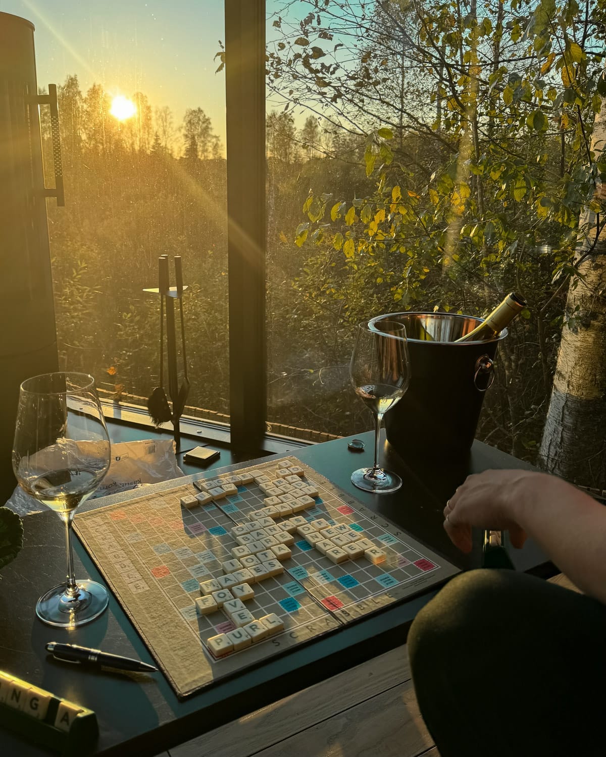 Sunset view from inside the glass-walled Kaseke cabin with wine glasses and a Scrabble board on the table.