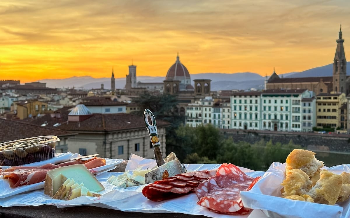 A sunset picnic of Italian cheeses and charcuterie overlooking the romantic city skyline of Florence, one of Europe's unforgettable travel destinations.