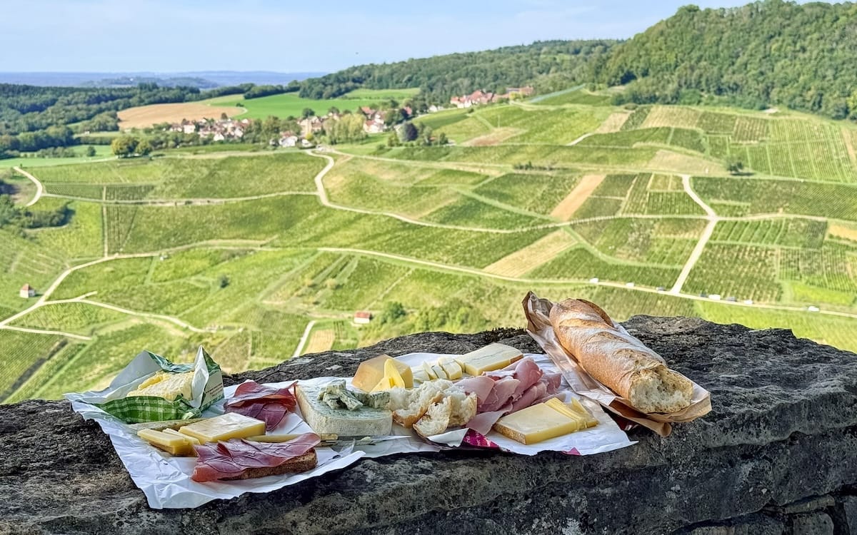 Picnic with Comté cheese and saucisson on a stone ledge above vineyards in Château-Chalon, one of the best things to do in Jura, France.